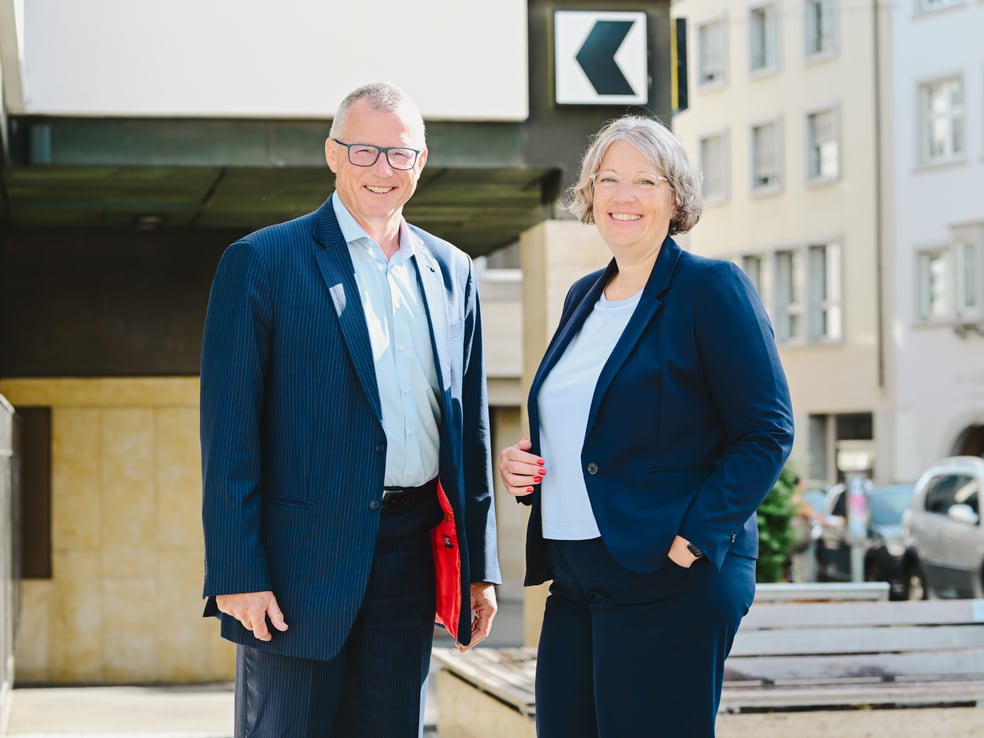Zwei Personen in Businesskleidung stehen draussen in einer urbanen Umgebung