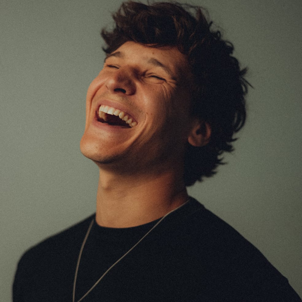 Wincent Weiss Stars in Town Person mit dunklem Haar lächelt glücklich vor neutralem Hintergrund.