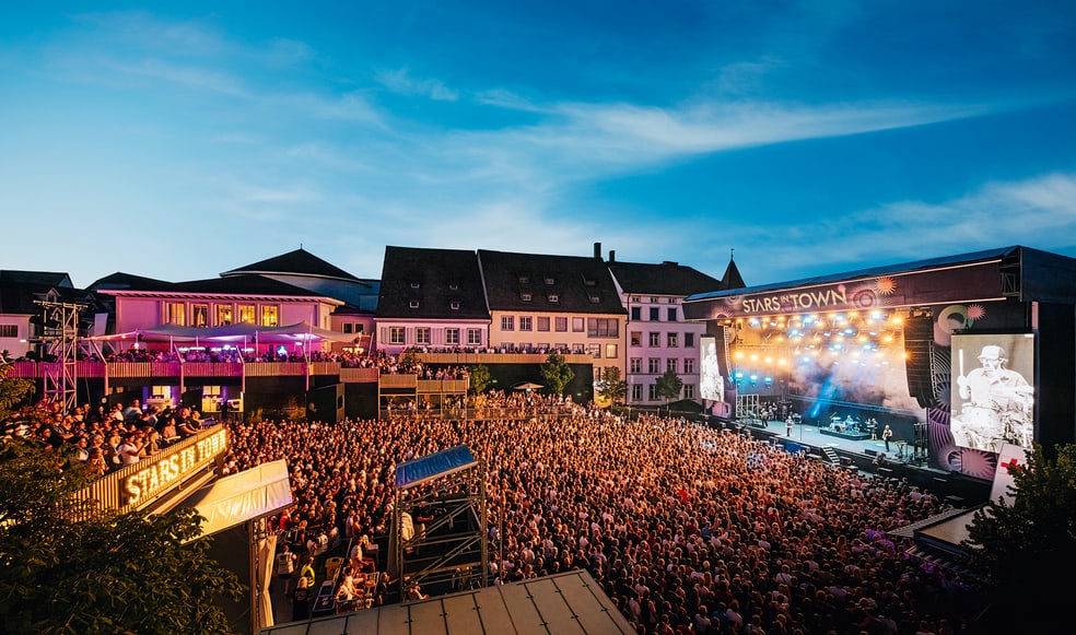 Grosses Outdoor-Konzert bei Sonnenuntergang mit Menschenmenge vor der Bühne.