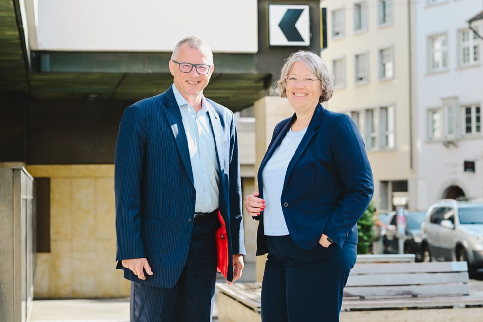 Zwei Personen in Businesskleidung stehen draussen in einer urbanen Umgebung