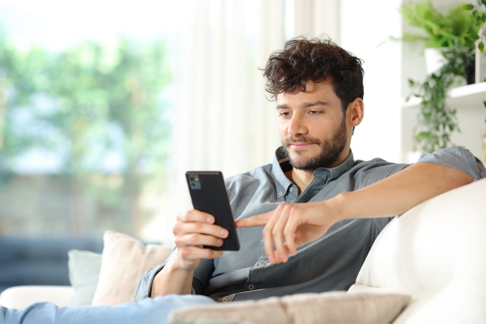 Herr sitzt auf dem Sofa und eröffnet sein Bankkonto digital